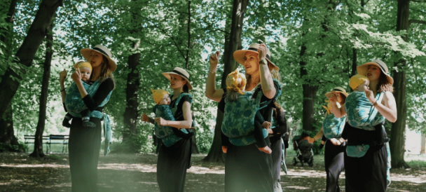grupa kobiet z grupy "chuśtaniec" z dziećmi w chustach stoi w parku w tanecznym układzie