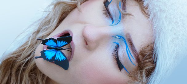 Portret kobiety z niebieskim motylem na ustach.
