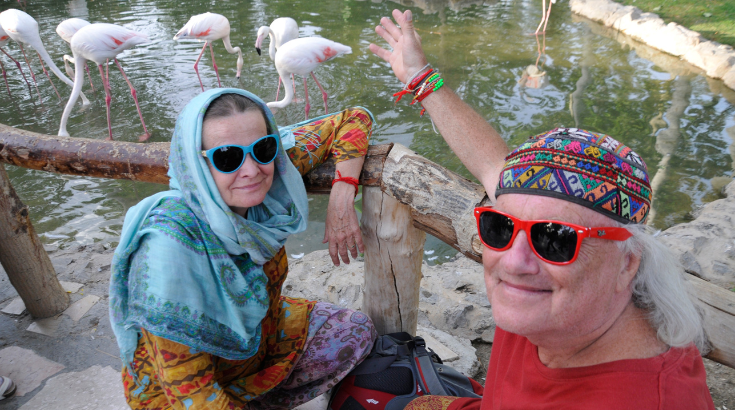 Mężczyzna o kobieta w nakryciach głowy i okularach przeciwsłonecznych na tle flamingów