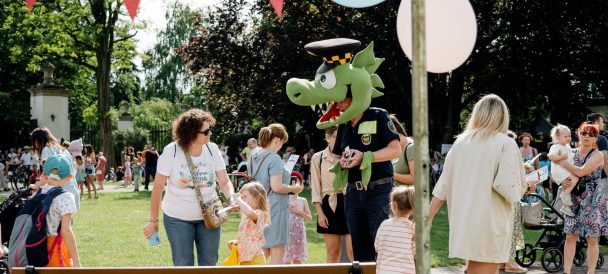 Smok Barbakus: fotografia maskotki straży miejskiej pośród dzieci na pikniku rodzinnym - plener Dworku Białoprądnickiego.