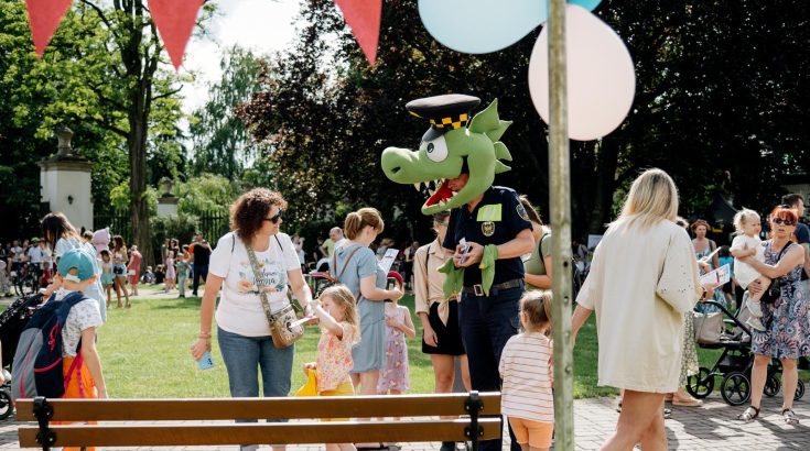 Smok Barbakus: fotografia maskotki straży miejskiej pośród dzieci na pikniku rodzinnym - plener Dworku Białoprądnickiego.