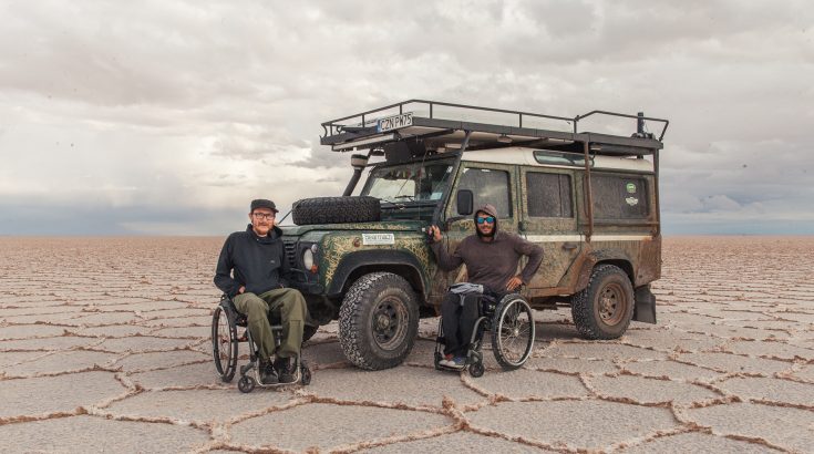 Dwóch mężczyzn na wózkach inwalidzkich przed autem off-roadowym.