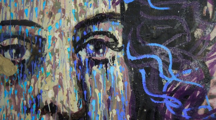 Mural przedstawiający górną połowę twarzy kobiety z bujnymi czarno-niebieskimi włosami o twarzy z wielokolorowymi plamkami.
