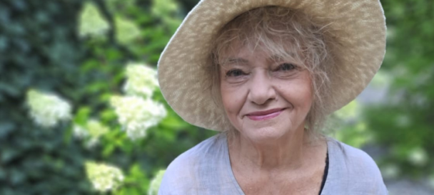 Uśmiechnieta kobieta w słomianym kapeluszu spogląda w obiektyw.