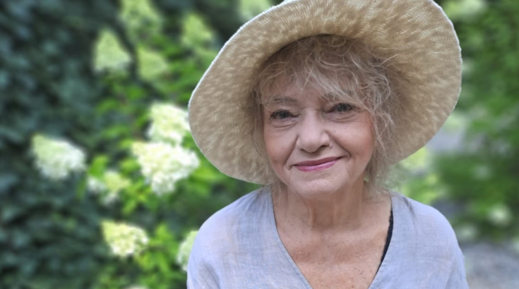 Uśmiechnieta kobieta w słomianym kapeluszu spogląda w obiektyw.