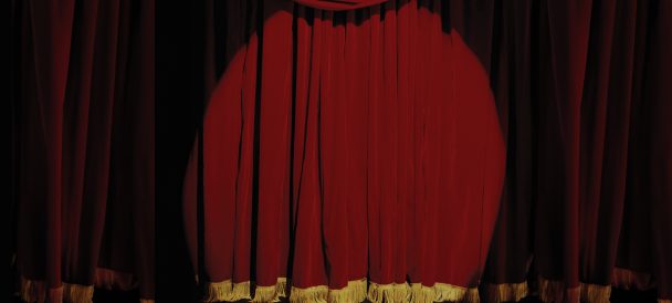 Światło rzucone na bordową, zasłoniętą kurtynę sceny teatralnej.