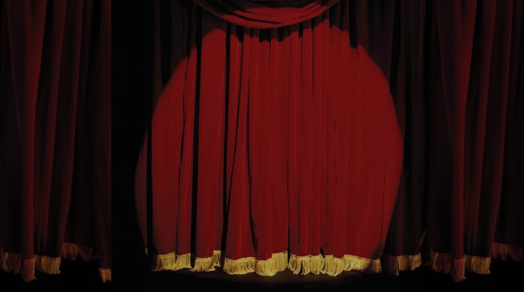 Światło rzucone na bordową, zasłoniętą kurtynę sceny teatralnej.