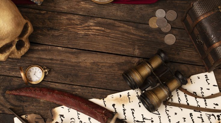 Pirackie akcesoria na deskach drewnianych: lornetka, monety, list, fragment szabli.