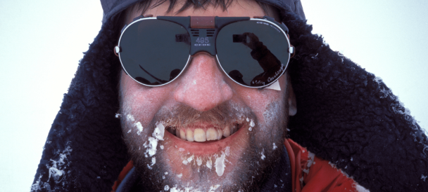 Uśmiechnieta twarz mężczyzny w zimowej czapce i okularach który na brodzie ma zamarznięte sople.