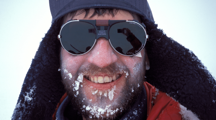 Uśmiechnieta twarz mężczyzny w zimowej czapce i okularach który na brodzie ma zamarznięte sople.