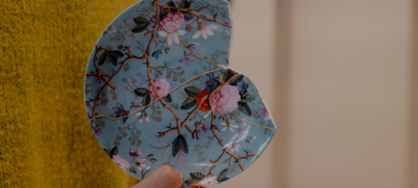 Na fotografii ktoś trzyma talerzyk niebieski w kwiaty ubity z jednej strony.