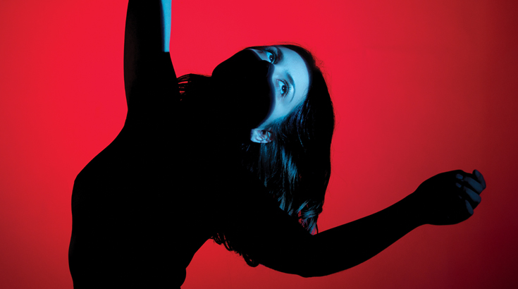 Postać kobiety w cieniu w pozie tanecznej na czerwonym tle.