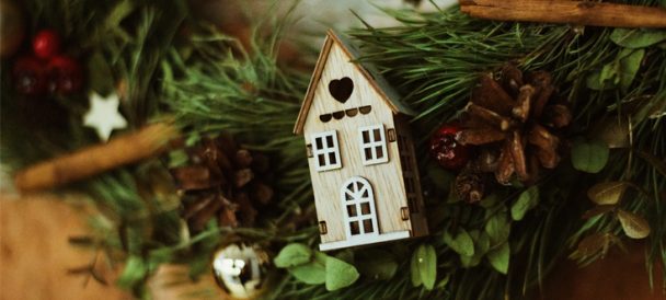 Na fotografii mały drewniany domek umieszczony na naturalnym igliwiu.