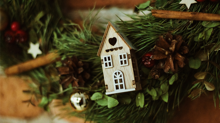 Na fotografii mały drewniany domek umieszczony na naturalnym igliwiu.