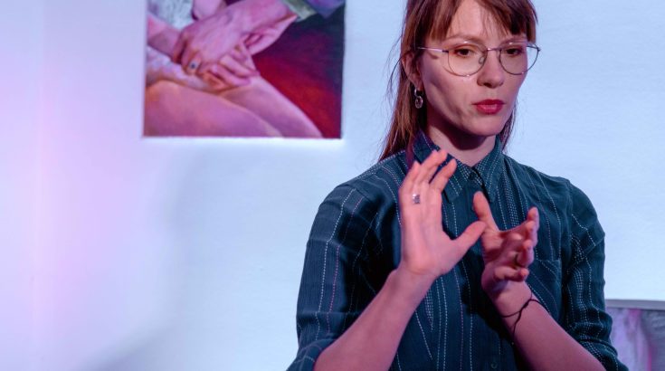 Mariia Varlygina, kuratorka Galerii Baszta w Dworku Białoprądnickim na tle obrazu Wojciecha Łubianki.