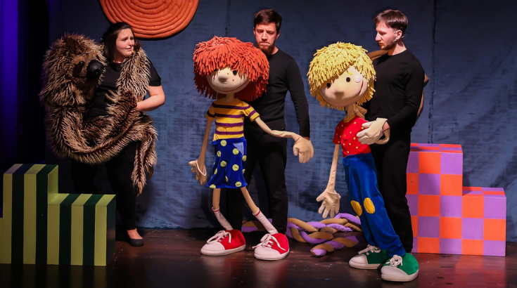 Na zdjęciu troje aktorów z lalkami wielkości dorosłego człowieka - chłopcem z blond włosami, chłopcem z rudymi włosami i wielkim wężem.