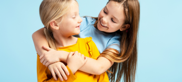 Dwie uśmiechnięte dziewczynki przytulają się niebieskim tle