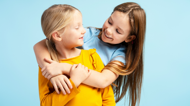 Dwie uśmiechnięte dziewczynki przytulają się niebieskim tle