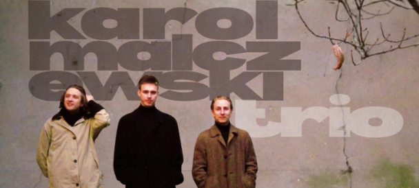 Na fotografii troje muzyków a za nimi na murze nazwa zespołu Karol Malczewski Trio.
