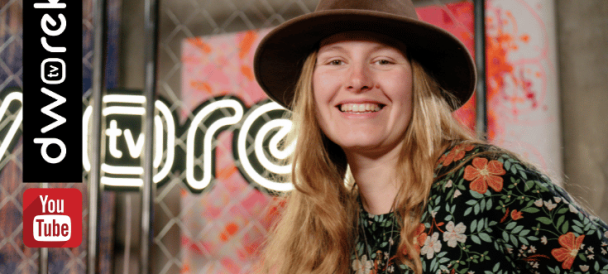 Uśmiechnięta kobieta z blond długimi włosami w kapeluszu na tle neonu dworek tv