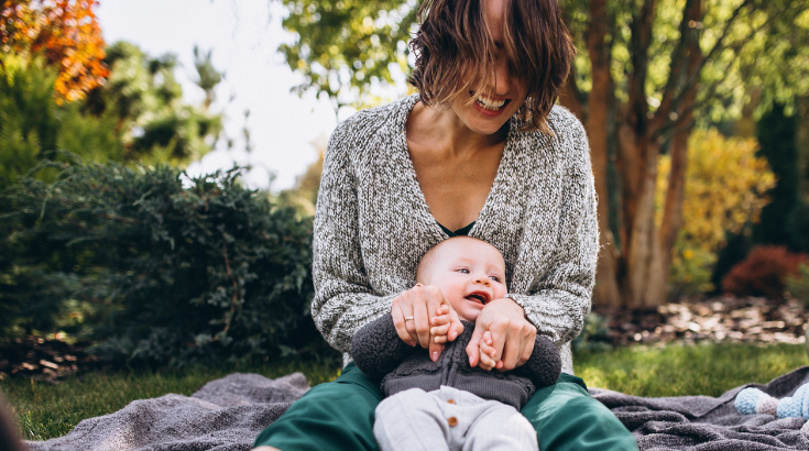 Roześmiana mama bawi się z niemowlakiem na kocu wśród drzew