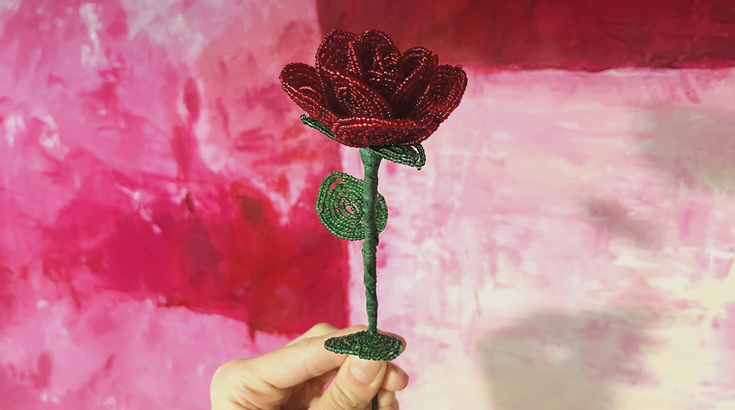 Na środku zdjęcia na biało czerwono różowym tle róża zrobiona w technice florystyki koralikowej