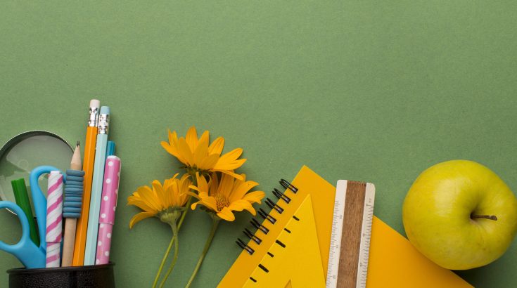 Notes, przybory papiernicze, jabłko i żółte kwiaty na zielonym tle.