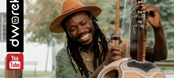 Na zdjęciu uśmiechnięty czarnoiskóry mężczyzna trzymający w ręku tradycyjny afrykański instrument.