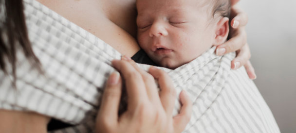 Niemowle zawiązane w chustę elastyczną śpi na mamie