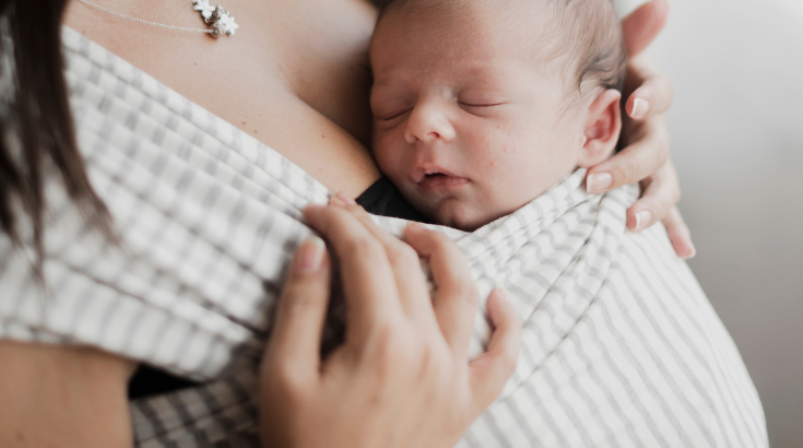 Niemowle zawiązane w chustę elastyczną śpi na mamie